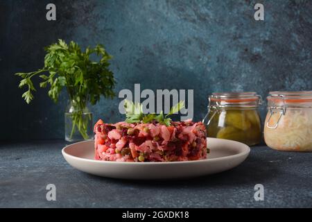 Vinegret ou vinaigrette. Salade rouge russe traditionnelle avec légumes cuits et marinés, petits pois, betteraves, en plaque blanche sur fond gris. Banque D'Images