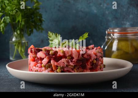 Vinegret ou vinaigrette. Salade rouge russe traditionnelle avec légumes cuits et marinés, petits pois, betteraves, en plaque blanche sur fond gris. Banque D'Images