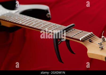 Guitare électrique fretboard avec capodoster, gros plan, fond rouge, personne. Instrument de musique à cordes, son électro, musique électronique, équipement pour Banque D'Images