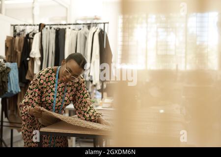 Jeune femme africaine de mode regardant le tissu dans son studio Banque D'Images