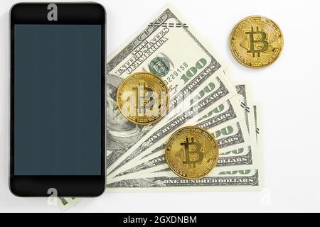 Pièces de monnaie en bitcoins et billets américains de cent dollars avec maquette de smartphone. Gros plan sur les pièces de monnaie crypto-monnaie en métal brillant bitcoin et le dollar américain Banque D'Images