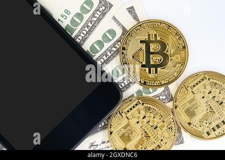 Vue de dessus bitcoins et billets américains de cent dollars avec smartphone. Gros plan sur les pièces de monnaie crypto-monnaie en métal brillant bitcoin et le dollar américain Banque D'Images