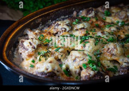 Boulettes de viande gratinées dans un plat à rôtir rustique avec du persil frais sur le dessus et l'herbe en arrière-plan Banque D'Images