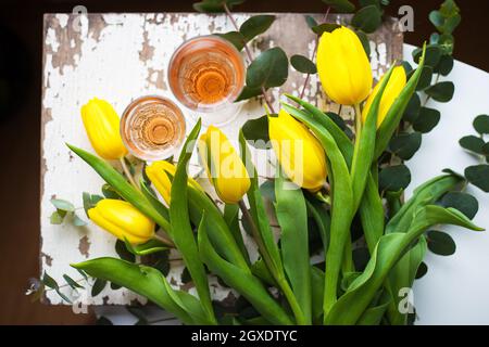 Tulipes jaunes sur un tableau blanc avec un verre de vin rose, close-up Banque D'Images