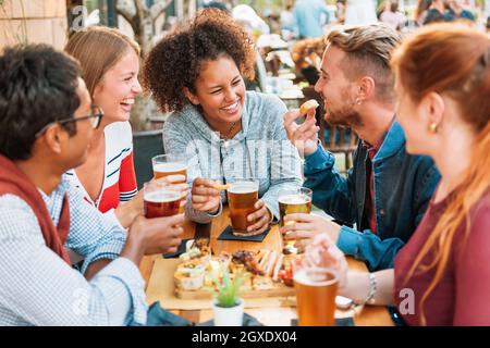 Groupe d'amis multiethniques divers s'amusant dans un pub en riant et en plaisantant sur des pintes de bière froide avec l'accent sur une jeune femme noire attrayante dans Banque D'Images