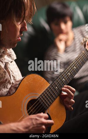 Le jeune musicien joue sa guitare acoustique comme ami dans l'arrière-plan écoute. Banque D'Images