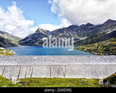 Barrage en béton et réservoir d'eau entouré de montagnes avec des pentes vertes sous ciel bleu ciel nuageux en été Banque D'Images