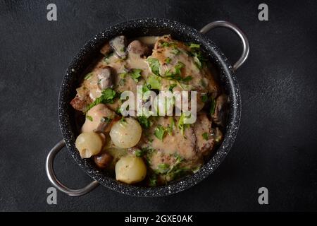 Fricassee - cuisine française. Poulet cuit dans une sauce crémeuse avec des champignons dans une casserole sur une table noire Banque D'Images