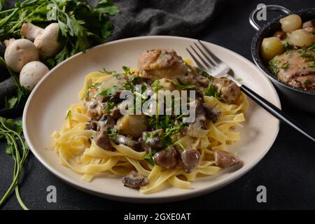 Fricassee - cuisine française. Poulet cuit dans une sauce crémeuse aux champignons dans une assiette blanche sur une table noire Banque D'Images