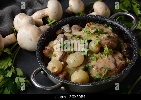 Fricassee - cuisine française. Poulet cuit dans une sauce crémeuse avec des champignons dans une casserole sur une table noire Banque D'Images