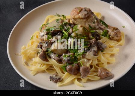 Fricassee - cuisine française. Poulet cuit dans une sauce crémeuse aux champignons dans une assiette blanche sur une table noire Banque D'Images