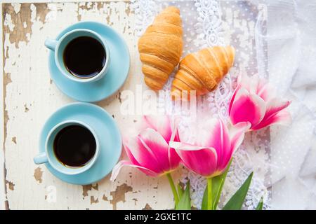 Bonne tasse de café, des croissants et des tulipes roses sur la vieille table blanche, close-up. Banque D'Images