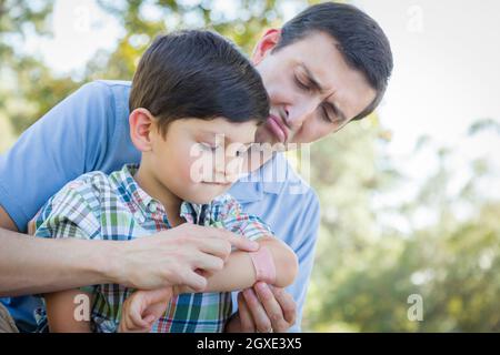 Père aimant met un bandage sur le coude de son jeune fils dans le parc. Banque D'Images