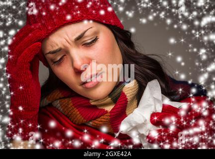 Sick Mixed Race femme portant un bonnet et des gants d'hiver avec un effet mouchoir et neige qui l'entoure. Banque D'Images