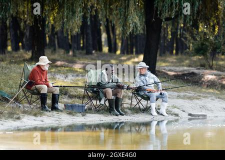 Souriant africain américain dans des bottes en caoutchouc pêche près des amis interraciaux et de la boîte à outils Banque D'Images