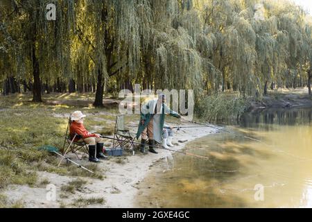 Homme afro-américain âgé pêchant dans l'eau du lac près des amis sur la côte Banque D'Images