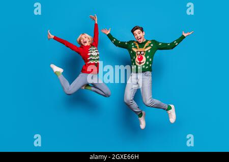 Pleine longueur de corps photo couple saut en laid chandail xmas isolé bleu vif fond de couleur. Banque D'Images