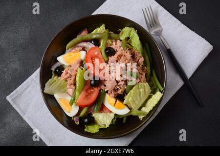 Salade niçoise. Cuisine française. Salade saine de thon, haricots verts, tomates, oeufs, pommes de terre, gros plan des olives noires dans un bol sur la table. Banque D'Images