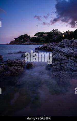 rochers sur la plage avec petite ville en arrière-plan au crépuscule et effet soie, blanes catalogne espagne Banque D'Images