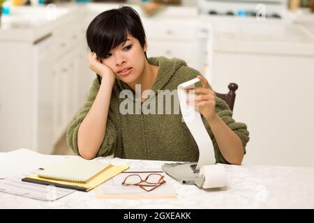 Jeune femme multi-ethnique tourmenter au sujet des calculs financiers dans sa cuisine. Banque D'Images