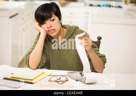 Jeune femme multi-ethnique tourmenter au sujet des calculs financiers dans sa cuisine. Banque D'Images