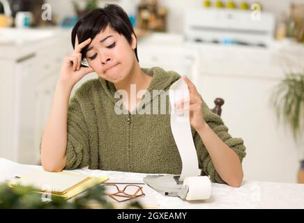 Jeune femme multi-ethnique tourmenter au sujet des calculs financiers dans sa cuisine. Banque D'Images