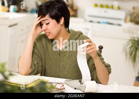 Jeune femme multi-ethnique tourmenter au sujet des calculs financiers dans sa cuisine. Banque D'Images