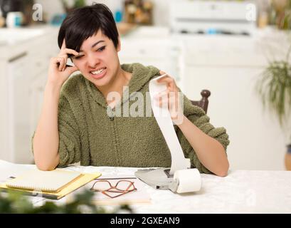 Jeune femme multi-ethnique tourmenter au sujet des calculs financiers dans sa cuisine. Banque D'Images