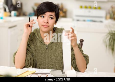 Jeune femme multi-ethnique tourmenter au sujet des calculs financiers dans sa cuisine. Banque D'Images