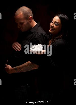 Fun Mixed Race Woman Holding Baby Shoes blanc contre un fond noir sous éclairage dramatique. Banque D'Images