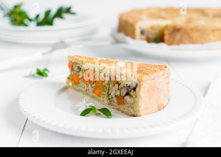 Libre d'un morceau de tarte de viande cuite au four avec des légumes, les carottes, les haricots rouges et les pois organisé sur plaque blanche et table en bois Banque D'Images
