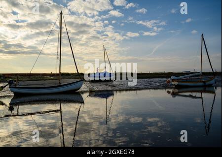 Un homme marche sur la rive avec des voiliers amarrés sur Morston Creek près de Blakeney point tandis que la marée monte sur une brillante fin d'après-midi. Norfolk, Angleterre. Banque D'Images