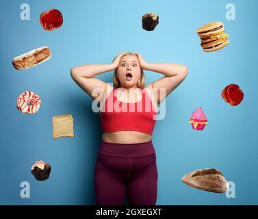 FAT girl dans la suite de fitness veut commencer un régime mais a des doutes sur la nourriture à acheter Banque D'Images