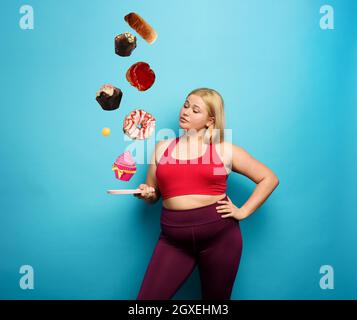 FAT fille essaie de jouer avec le tennis de table mais pense toujours à manger. Banque D'Images