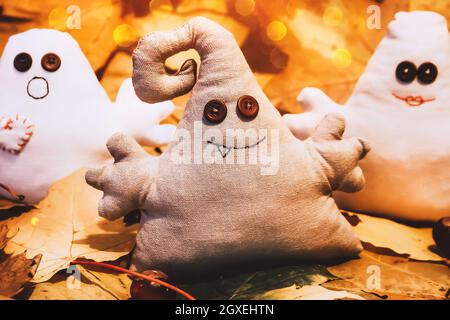 Monstres jouets avec des yeux de bouton parmi les feuilles et les bougies d'automne. Carte de vacances d'Halloween et décoration de maison avec lumières floues bokeh Banque D'Images