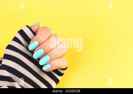 Femme main en chemise à rayures marin avec une belle manucure - ongles bleu menthe sur fond jaune avec espace de copie Banque D'Images