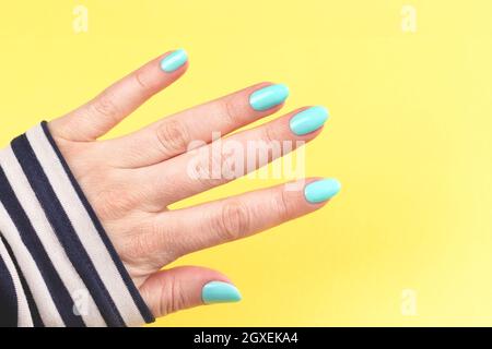 Femme main en chemise à rayures marin avec une belle manucure - ongles bleu menthe sur fond jaune Banque D'Images