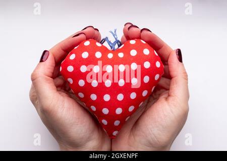 Mains de femme avec coeur rouge en tissu doux et clous scintillants rouge foncé sur fond blanc. Banque D'Images