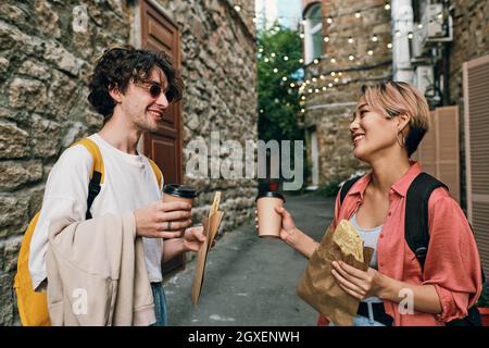 Les jeunes sont heureux avec des boissons et des en-cas qui se regardent les uns les autres en se tenant dans la rue Banque D'Images