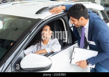 Jolie dame assise à l'intérieur de la voiture, ayant une conversation avec un vendeur Banque D'Images