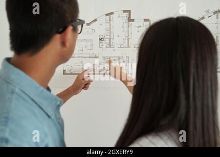 Vue arrière de deux jeunes architectes pointant vers un grand croquis sur le mur Banque D'Images