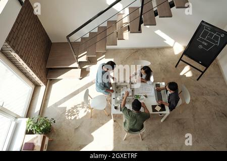 Groupe de jeunes architectes chinois réunis par table pour discuter des idées de leur nouveau projet Banque D'Images