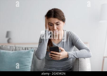 Une jeune femme européenne triste et choquante, souffrant de dépression, est assise sur un canapé et lit un message Banque D'Images