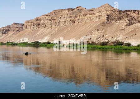 Deux pêcheurs dans un petit bateau sur le Nil très petit dans le vaste reflet des montagnes désertiques derrière Banque D'Images