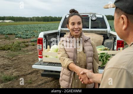 Bonne femme d'affaires qui secoue la main d'un fermier mûr contre la voiture et le champ de chou Banque D'Images