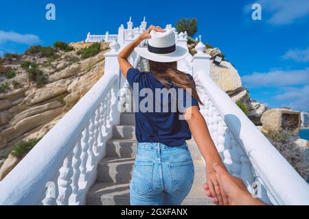 Jeune touriste femme dans le chapeau blanc de soleil dirigeant l'homme à la main. Suivez-moi. Balcon del Mediterraneo, Benidorm, Espagne. Couple en vacances d'été Banque D'Images