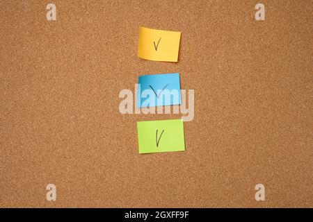 autocollants en papier colorés collés sur un panneau en liège marron, gros plan Banque D'Images