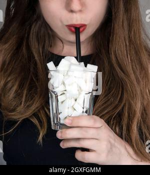 Portrait d'une jeune femme qui boit avec une paille noire d'un verre rempli de cubes de sucre Junk food, régime malsain, trop de sucre sur les boissons, Banque D'Images