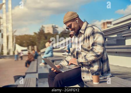 Jeune homme hippster est assis à l'extérieur avec le café tout en vérifiant l'e-mail, le travail, blogging, étudiant en ligne Banque D'Images