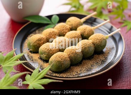 Boulettes de riz aromatisées à l'armoise recouvertes de farine de soja et de thé vert servies sur une assiette noire placée sur un plateau rouge boulettes japonaises. Banque D'Images